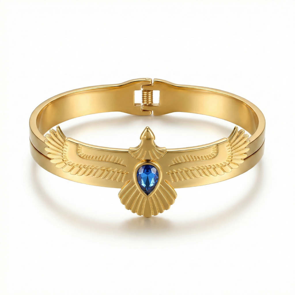 Brazalete rígido de acero bañado en oro de 18K con diseño de ave de alas extendidas y piedra central azul, fabricado en España.