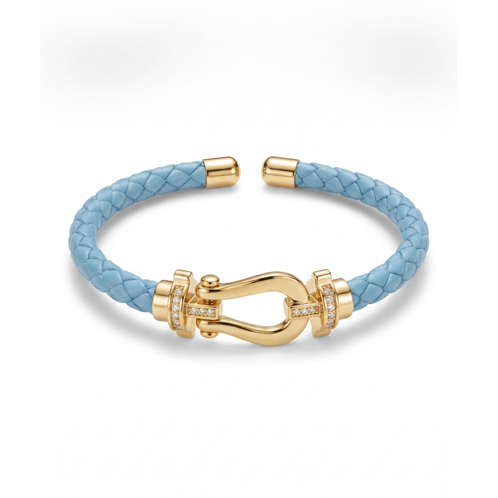 Pulsera trenzada de piel en color azul celeste con cierre estilo herradura bañado en oro de 18K y detalles de circonitas brillantes. Joyería fabricada en España.