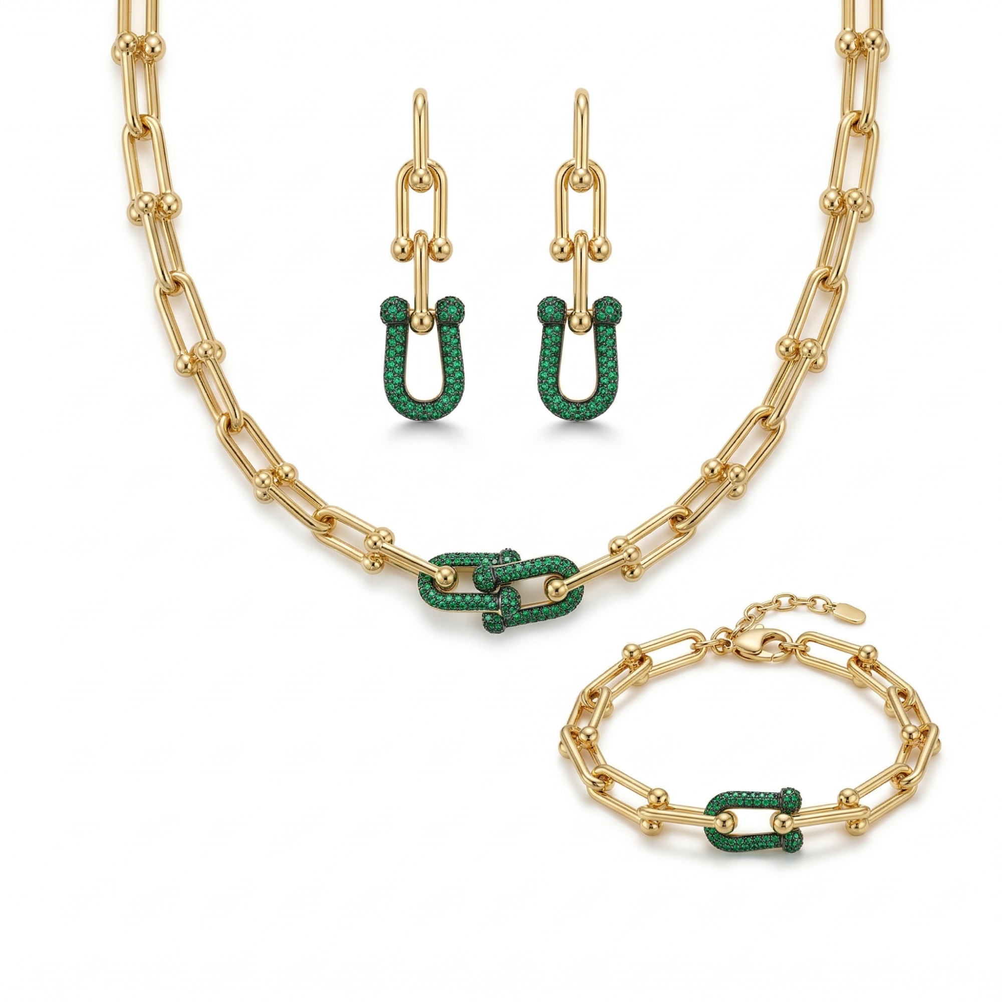 Un conjunto de joyas de lujo de acero bañado en oro de 18K, compuesto por un collar de cadena de eslabones gruesos, una pulsera a juego y un par de pendientes largos. Cada pieza tiene un diseño central de eslabones entrelazados adornados con pavé de piedras verdes brillantes, fabricado en Italia.