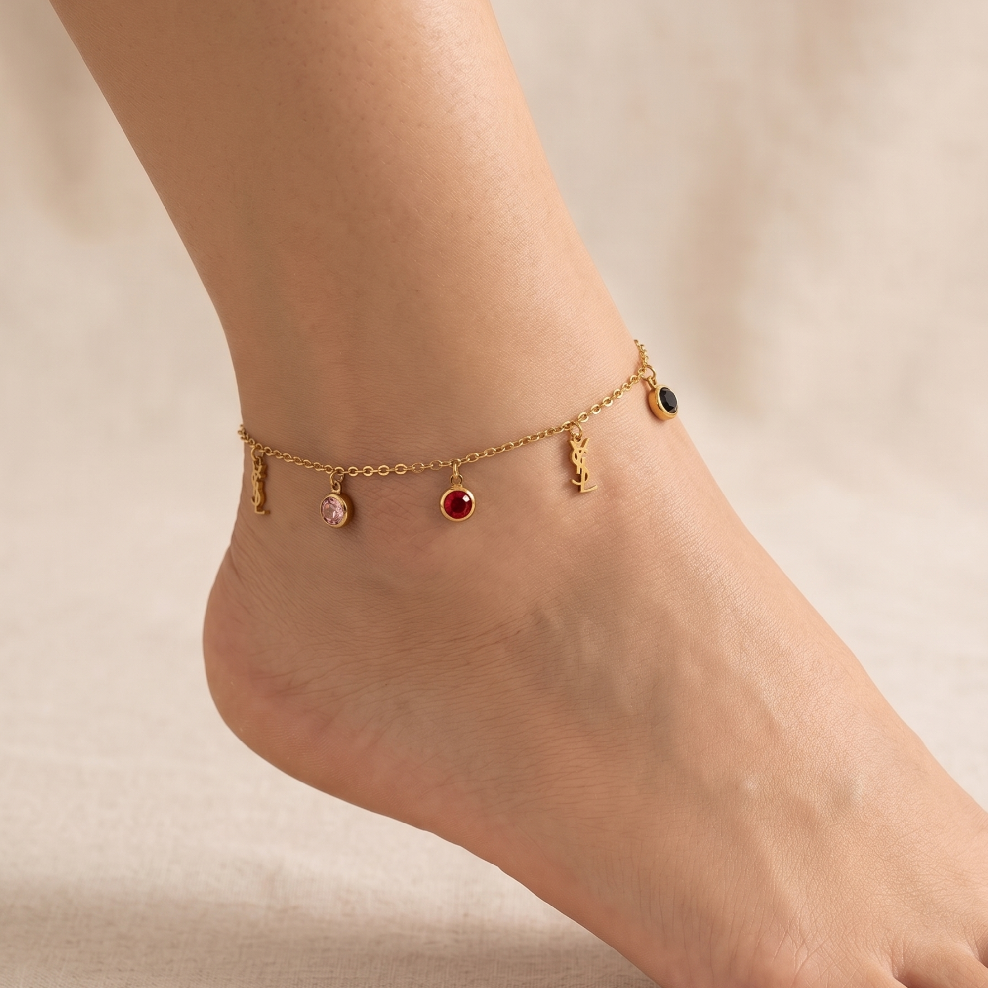 Tobillera de cadena fina de acero con baño de oro de 18K, adornada con charms colgantes de cristales de colores arcoíris y símbolos dorados, hecha en España.